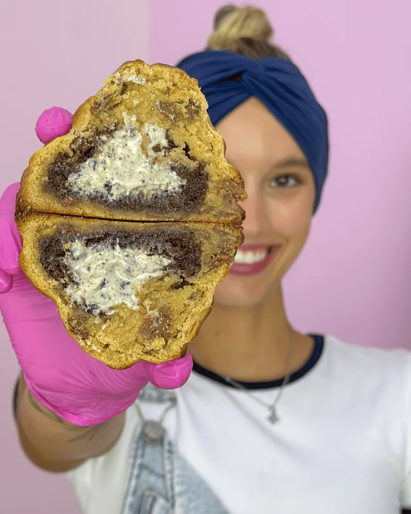 Nikh segurando um cookie partido ao meio, com luva rosa
